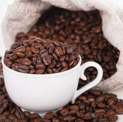 Coffee cup with burlap sack of roasted beans on rustic table