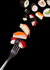 Sushi pieces falling on fork, isolated on black background