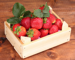 Strawberries with leaves in wooden box on wooden  background