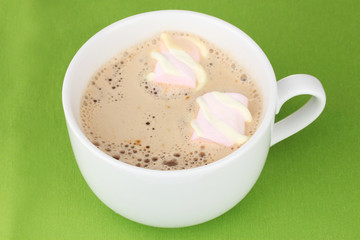 Cup of cappucino with marshmallows on green background