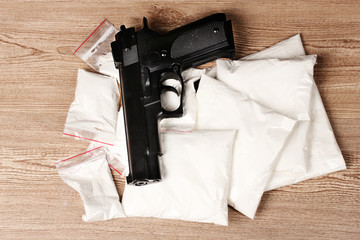 Cocaine in packages and handgun on wooden background