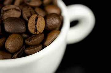Close up photograph of brown coffee beans in a white mug.