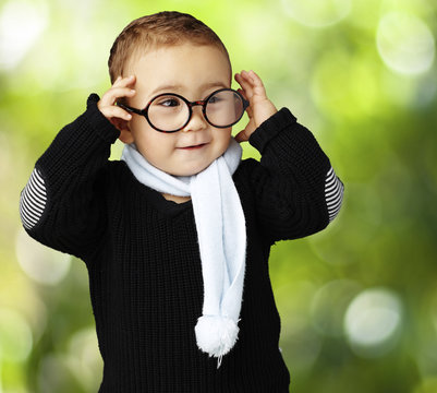 portrait of funny kid holding his glasses  against a nature back