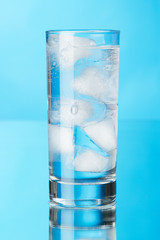 Glass of ice water on blue background
