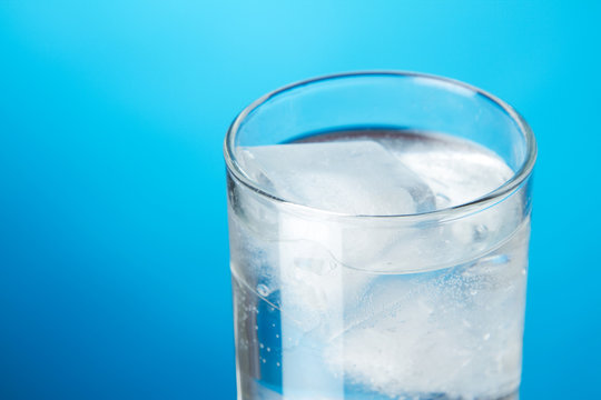 Glass of ice water on blue background