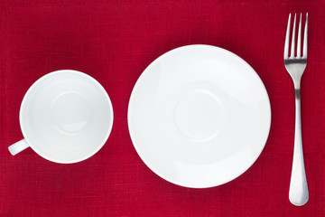 Cup, plate and fork on red background