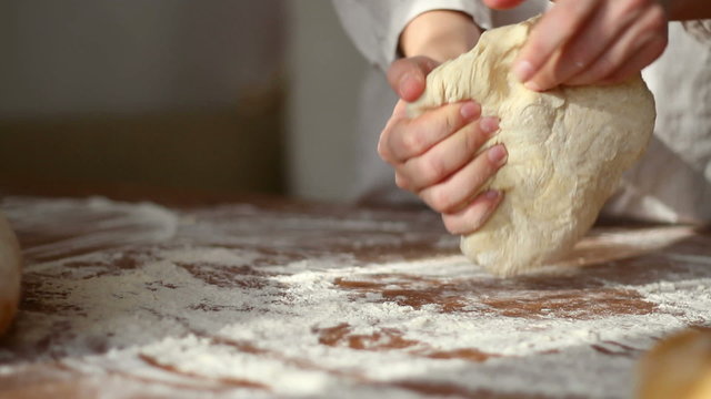 Female hands kneading dough in flour on table, dolly shot