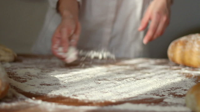 Baker kneading dough in flour on table, slow motion, dolly shot