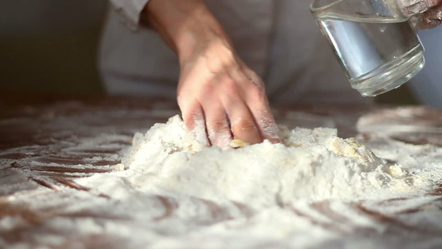 Baker adding water to flour on table, slow motion, dolly shot