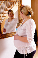 Hochschwangere Frau betrachtet sich im Spiegel