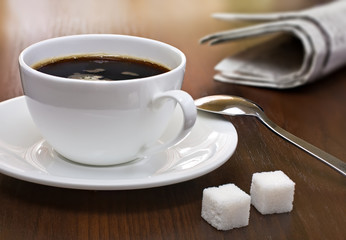 Coffee cup, lump sugar and newspapers on a table