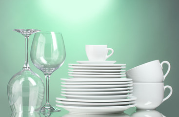 Clean plates, cups and glasses on green background