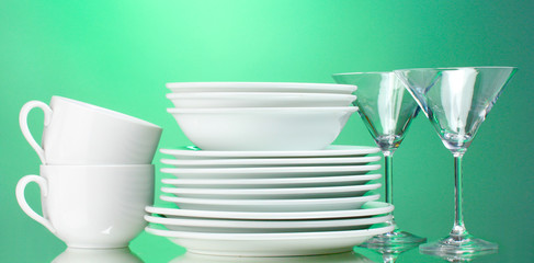 Clean plates, cups and glasses on green background