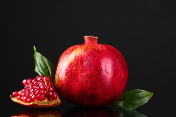 ripe pomegranate fruit with leaves on black background