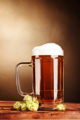 beer mug and green hop on wooden table on brown background