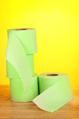 green rolls of toilet paper on wooden table on yellow background
