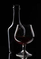 Glass of brandy and bottle on black background
