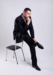 Elegant young businessman sitting on a chair and thinking - obrazy, fototapety, plakaty