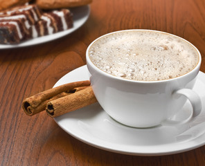 Cappuccino with cinnamon bark and plate of sweets