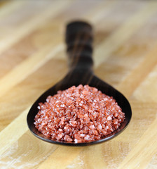 Red Hawaiian sea salt in a wooden spoon on a wooden table.
