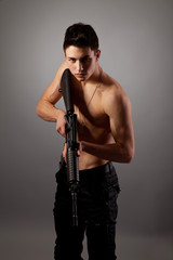 Fototapeta premium Handsome bare-chested soldier is holding a rifle