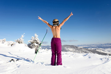 Rear view of female skier posing topless on mountain slope