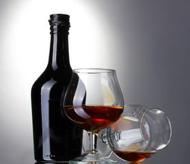 Glasses of brandy and bottle on gray background
