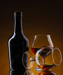Glasses of brandy and bottle on brown background