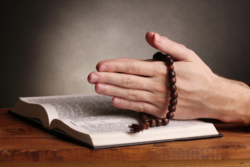 Hands holding wooden rosary over open russian holy bible