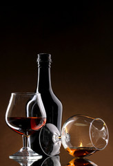 Glasses of brandy and bottle on brown background