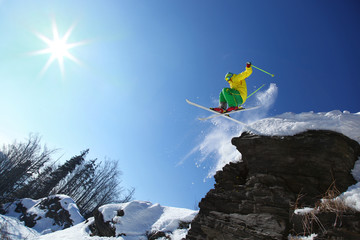 Cool skier jumping against blue sky from the rock