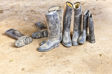 dirty plastic riding boots standing at the muddy gry ground