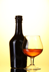 Glass of brandy and bottle on yellow background