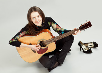 Fototapeta premium Attractive brunette girl playing guitar sitting on the floor
