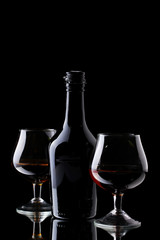 Glasses of brandy and bottle on black background