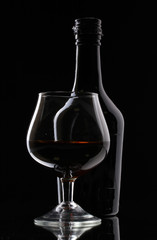 Glass of brandy and bottle on black background