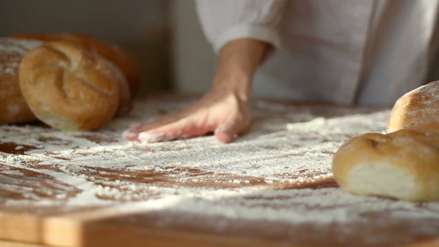 Baker hand throwing flour on the table and kneading dough