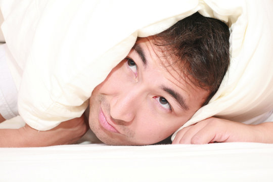 Man trying to sleep with a pillow over his head and close to wak
