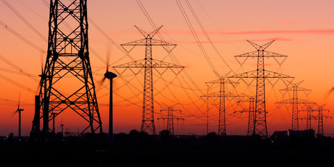 Strommasten bei Sonnenuntergang mit Windrädern