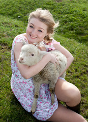 Young pretty cheerful blond woman with lamb on a countryside