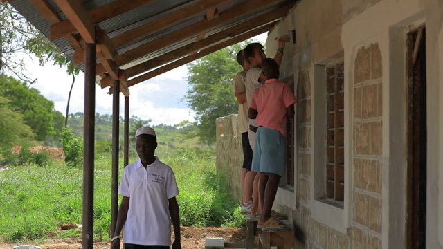 Painting the exterior of a school in a village in Kenya, volunteer and student, humanitarian work.