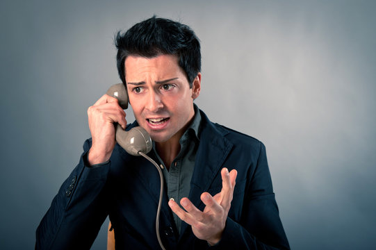 Angry man talking at the phone against grey background.