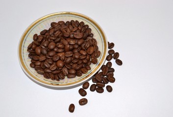 Coffee grains lie on a saucer on a white background