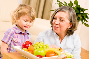 Grandmother with granddaughter eat fruit at home