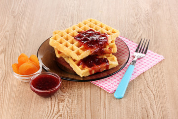 Tasty waffles with jam on plate on wooden background