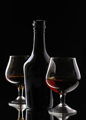Glasses of brandy and bottle on black background