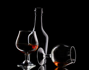 Glasses of brandy and bottle on black background