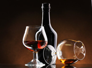 Glasses of brandy and bottle on brown background