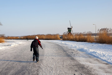 Boy is ice skating in dutch landscape