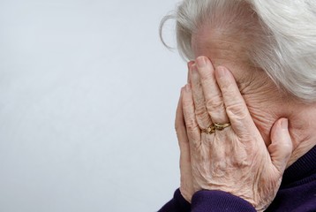 A crying elderly woman covering her face - Powered by Adobe